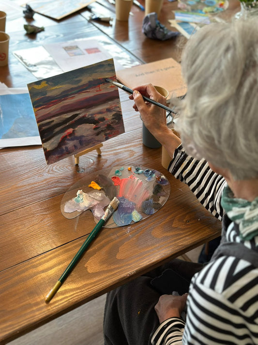 A workshop guest painting a sunset seascape on a small easel at a Lucy Kent painting workshop
