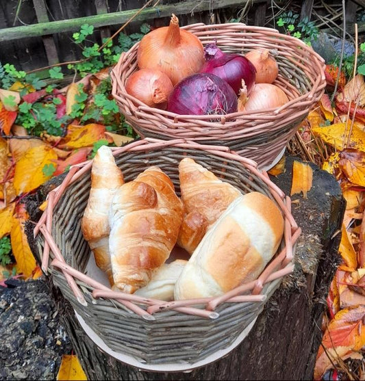 Two handwoven willow baskets filled with onions and croissants